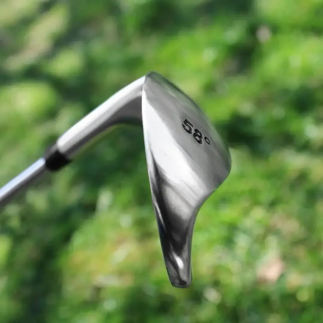 Close-up of a 58-degree silver golf sand wedge with wide sole on green grass background