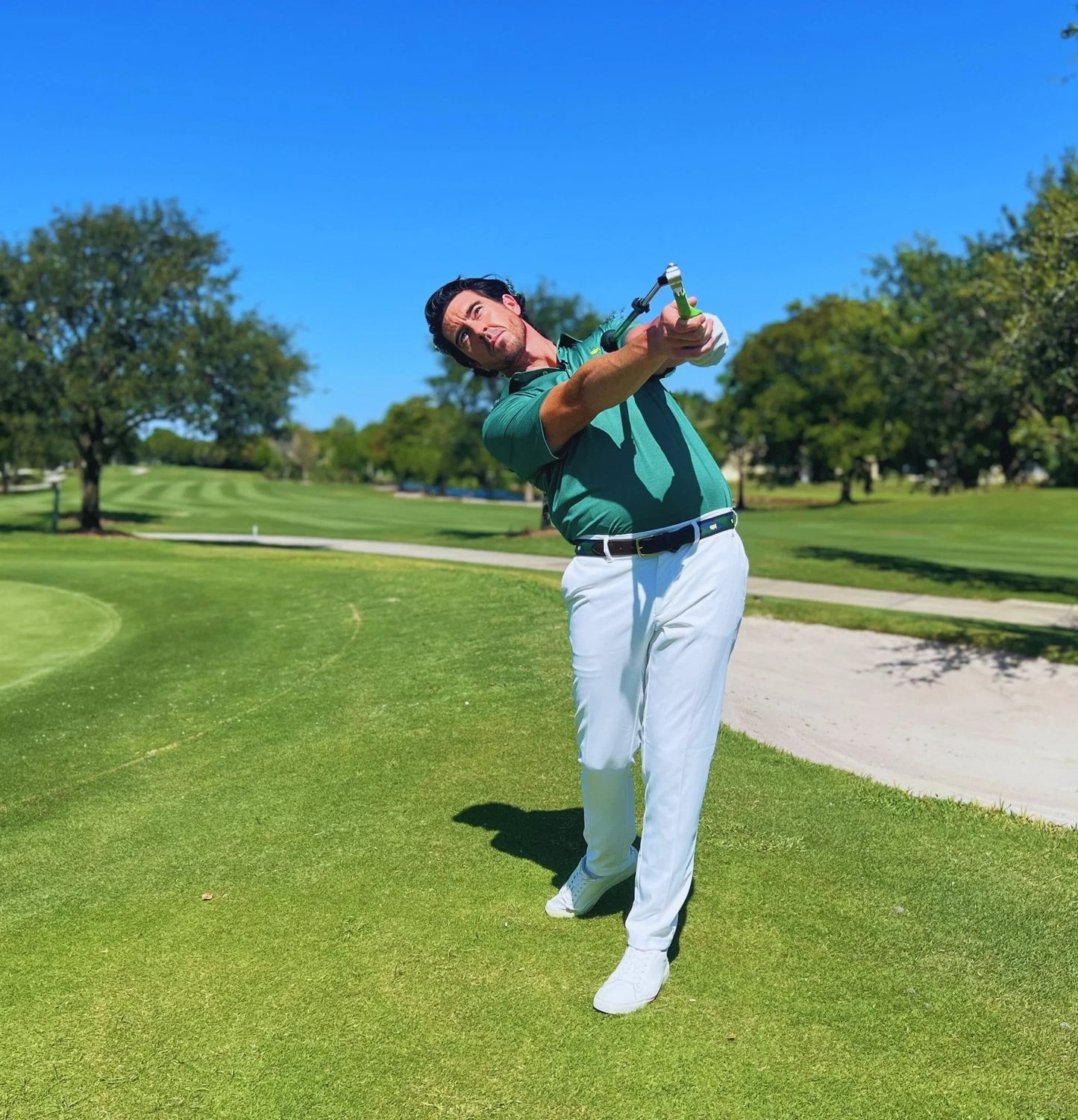 Golfer practicing swing with Sure Strike training aid on sunny golf course green