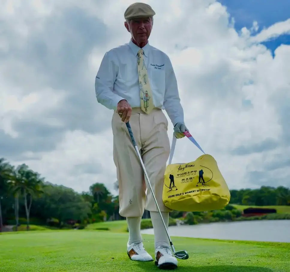 Elderly golfer on green fairway holding golf club and yellow Gary Wiren Impact Bag for golf training