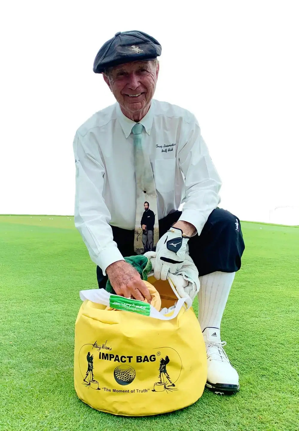elderly man in golf attire kneeling on green grass with yellow golf impact bag