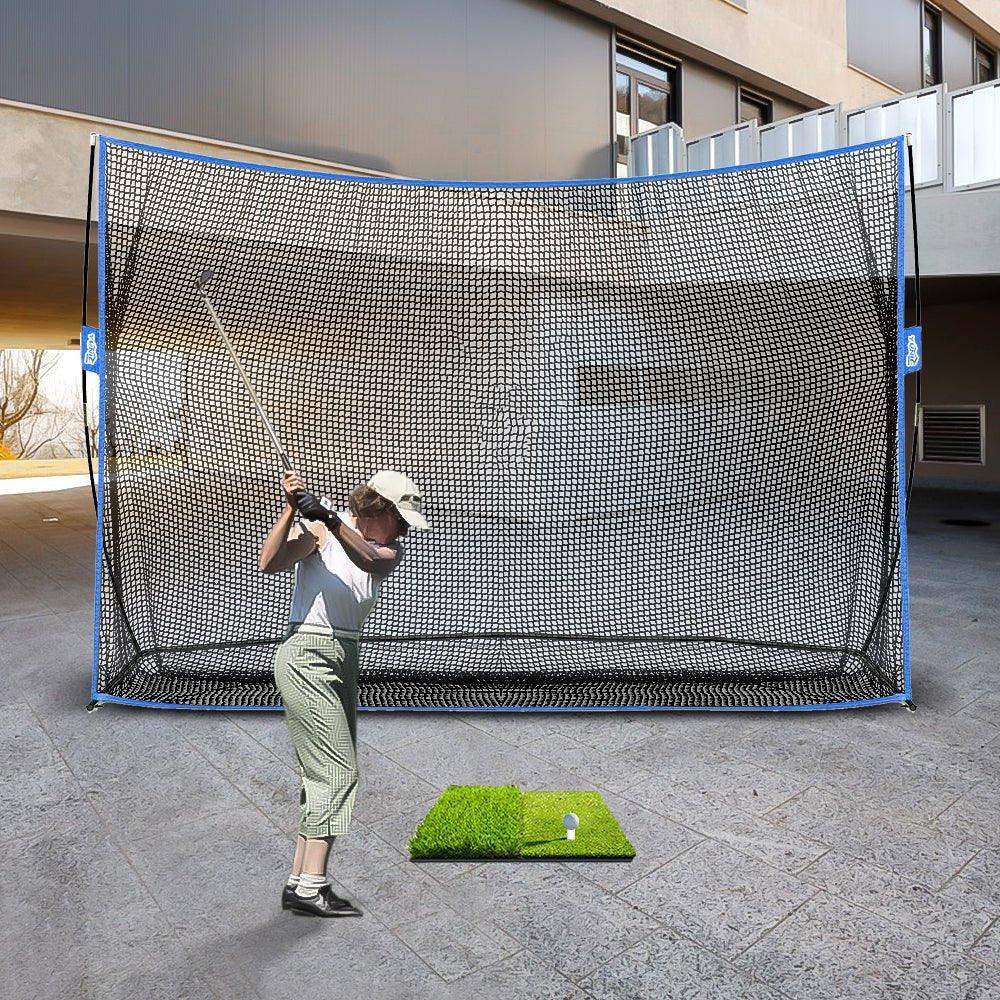 Golf practice net setup outdoors with golfer swinging club and golf ball on turf mat