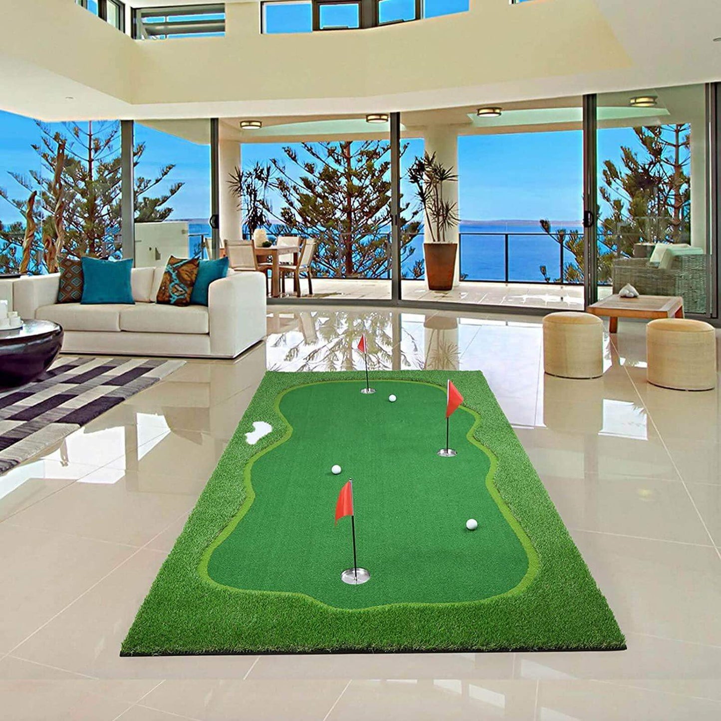 Indoor green golf putting mat with red flags and golf balls in modern living room with ocean view