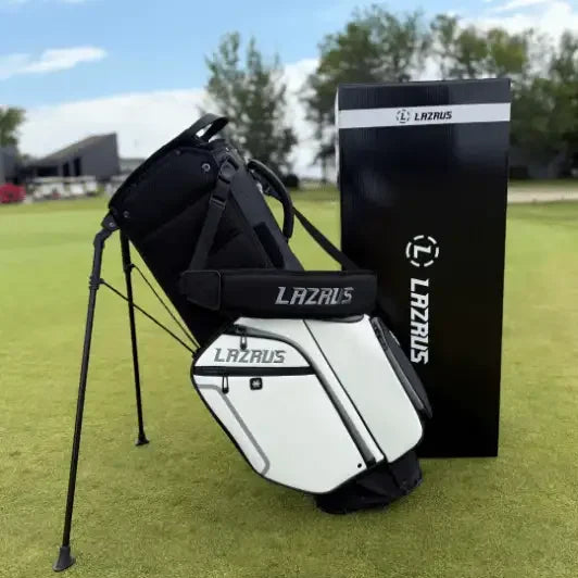 Lazrus branded white and black golf bag with stand on green grass next to Lazrus product box under clear sky