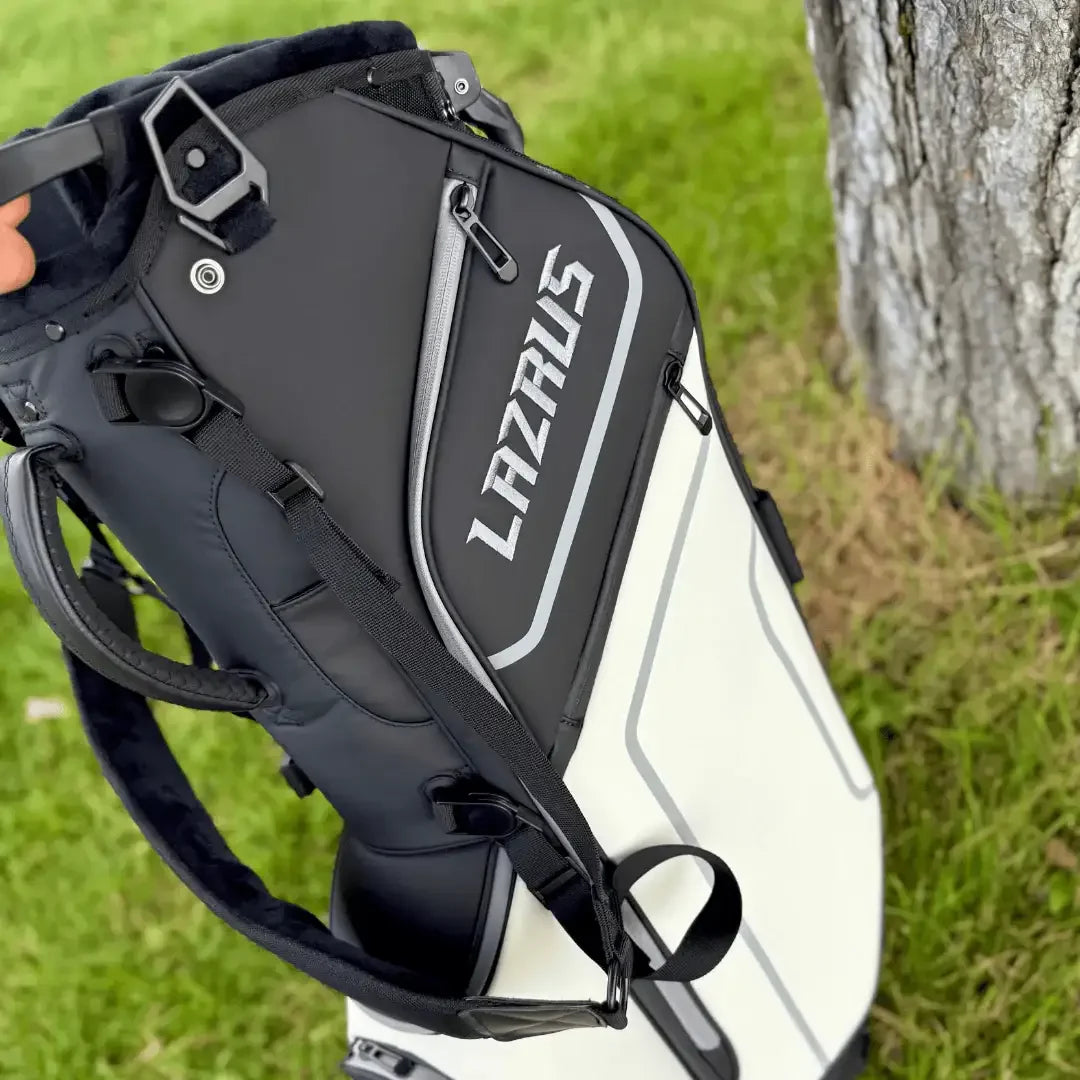 Black and white Lazrus golf bag with zippers and straps near a tree on green grass