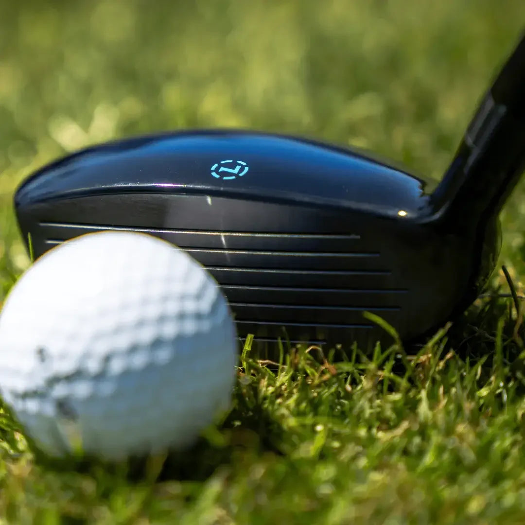 Close-up of black golf driver and white golf ball on green grass outdoors
