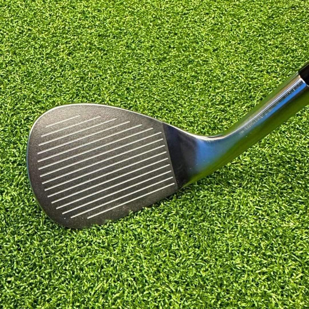 Close-up of a forged golf wedge club head lying on vibrant green artificial turf