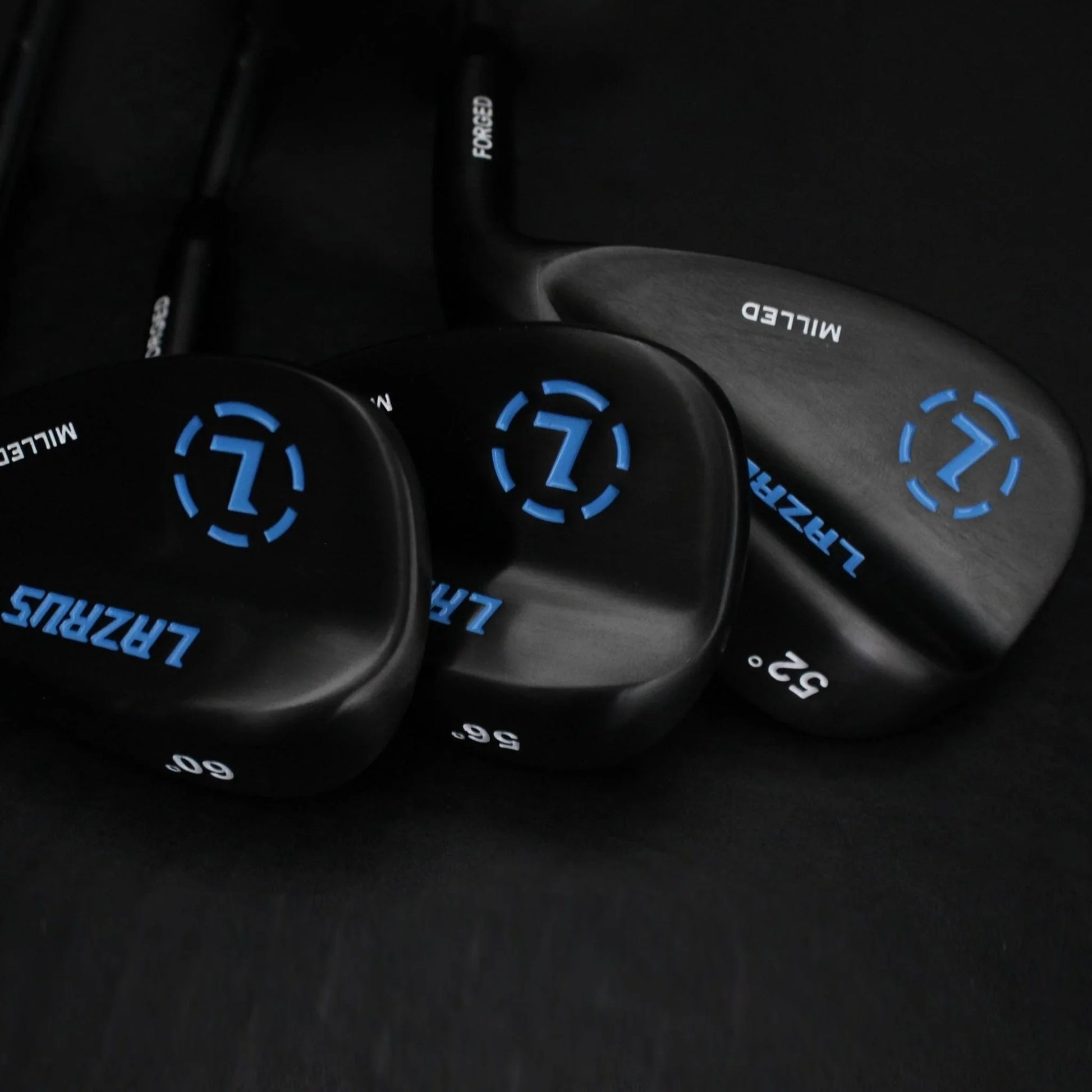 Set of black Lazrus forged golf wedges with blue logos and loft numbers 52, 56, 60 degrees on a dark background