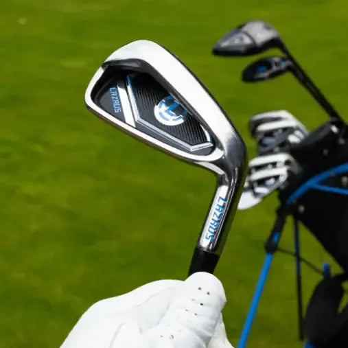 Close-up of Lazrus golf iron club held by gloved hand with golf bag and clubs on green grass