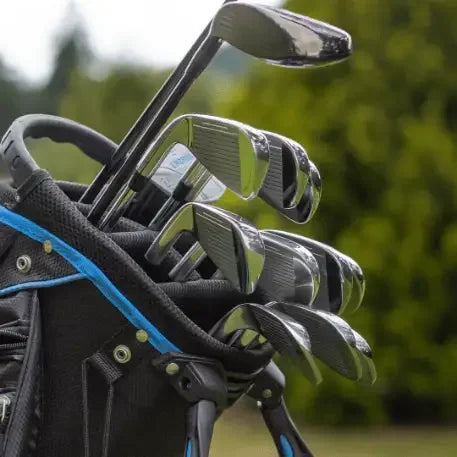 Set of shiny golf irons with black grips in a black and blue golf bag outdoors