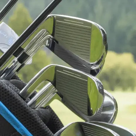 Close-up of shiny steel golf irons in a black and blue golf bag with a blurred green outdoor background
