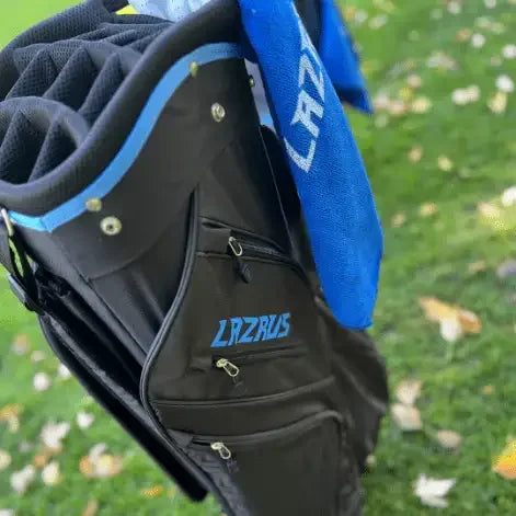 Black Lazrus premium golf bag with blue accents and Lazrus towel on grass with fallen leaves
