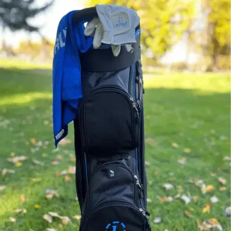 Black Lazrus golf bag with gloves and blue towel on green lawn with autumn trees