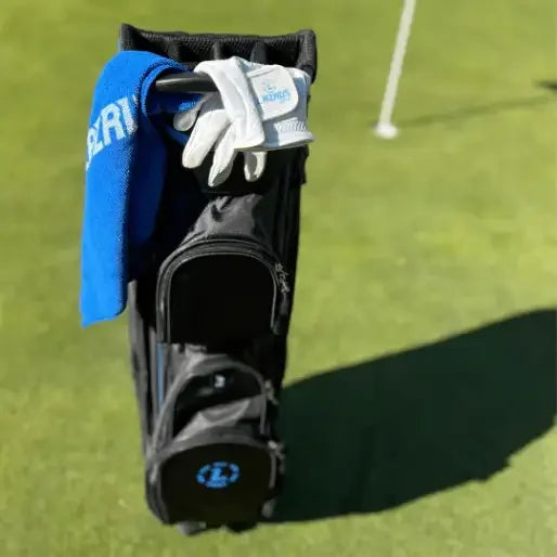 Black Lazrus golf bag with blue towel and white glove on green golf course near hole