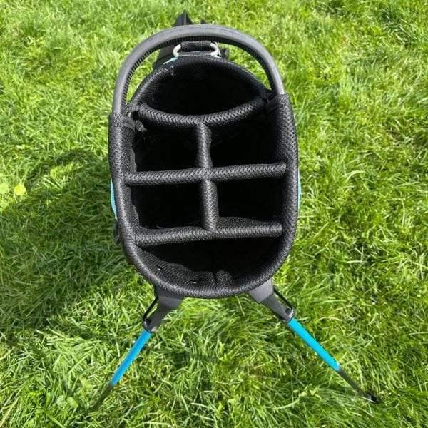 Top view of a black golf bag with multiple compartments standing on green grass with blue legs
