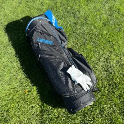 Black Lazrus premium golf bag with blue accents and a white golf glove on green grass