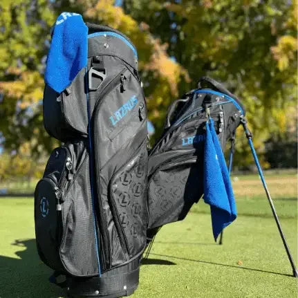 Two Lazrus premium black golf bags with blue accents and towels on a green golf course