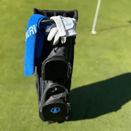 Black Lazrus golf bag standing on green with golf glove and blue towel hanging on side