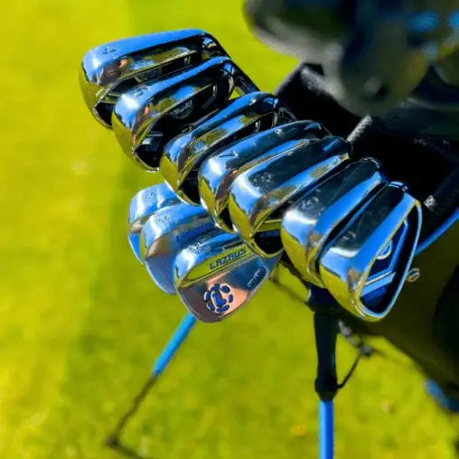 Set of Lazrus golf irons in a black bag on green grass, showing polished metal club heads