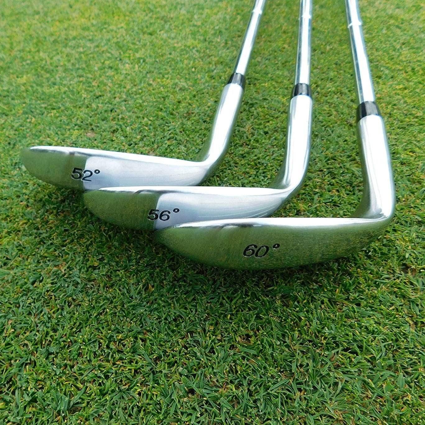 Set of three polished golf wedges with 52°, 56°, and 60° lofts on green grass