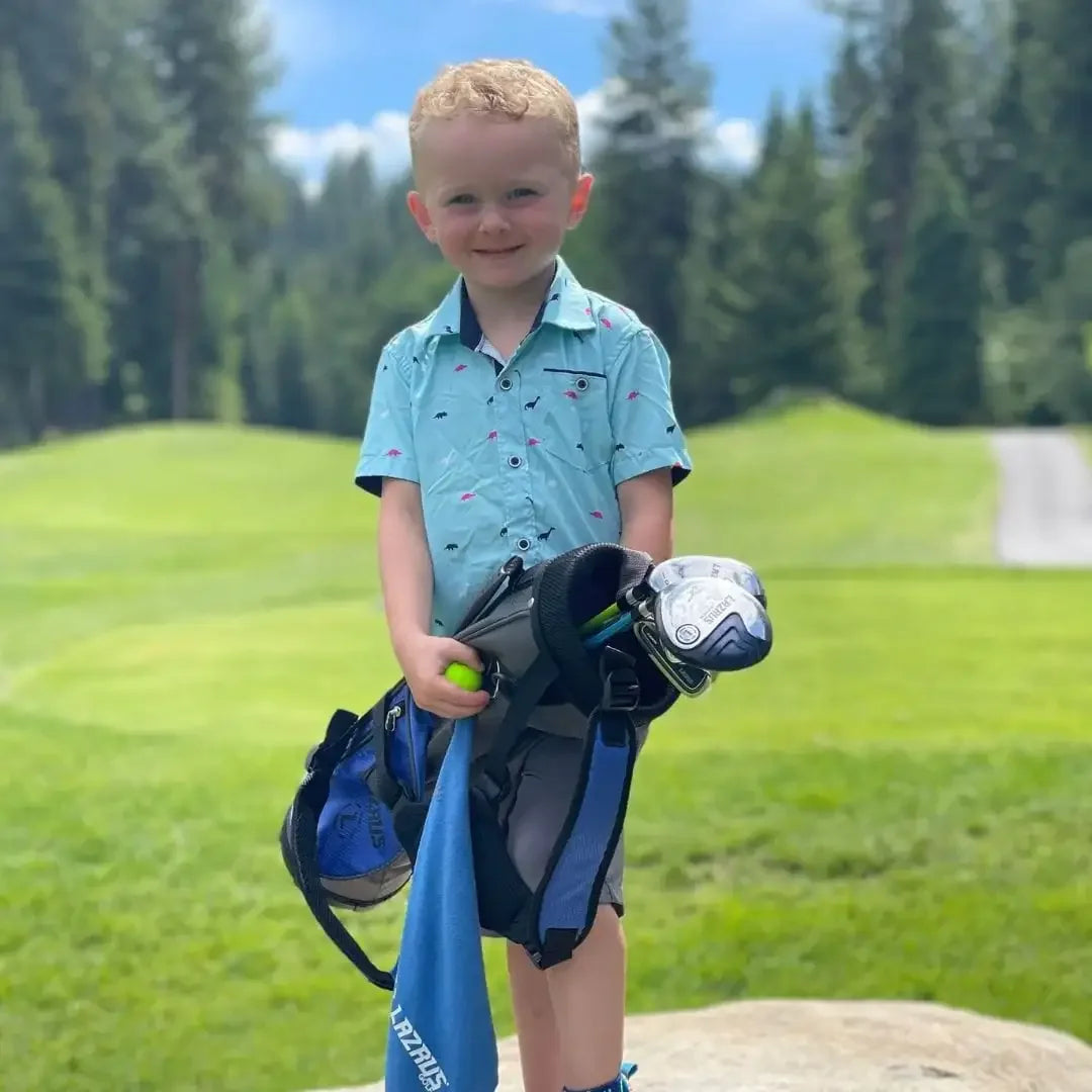 Young boy in blue shirt holding Lazrus junior golf clubs and green golf ball on golf course