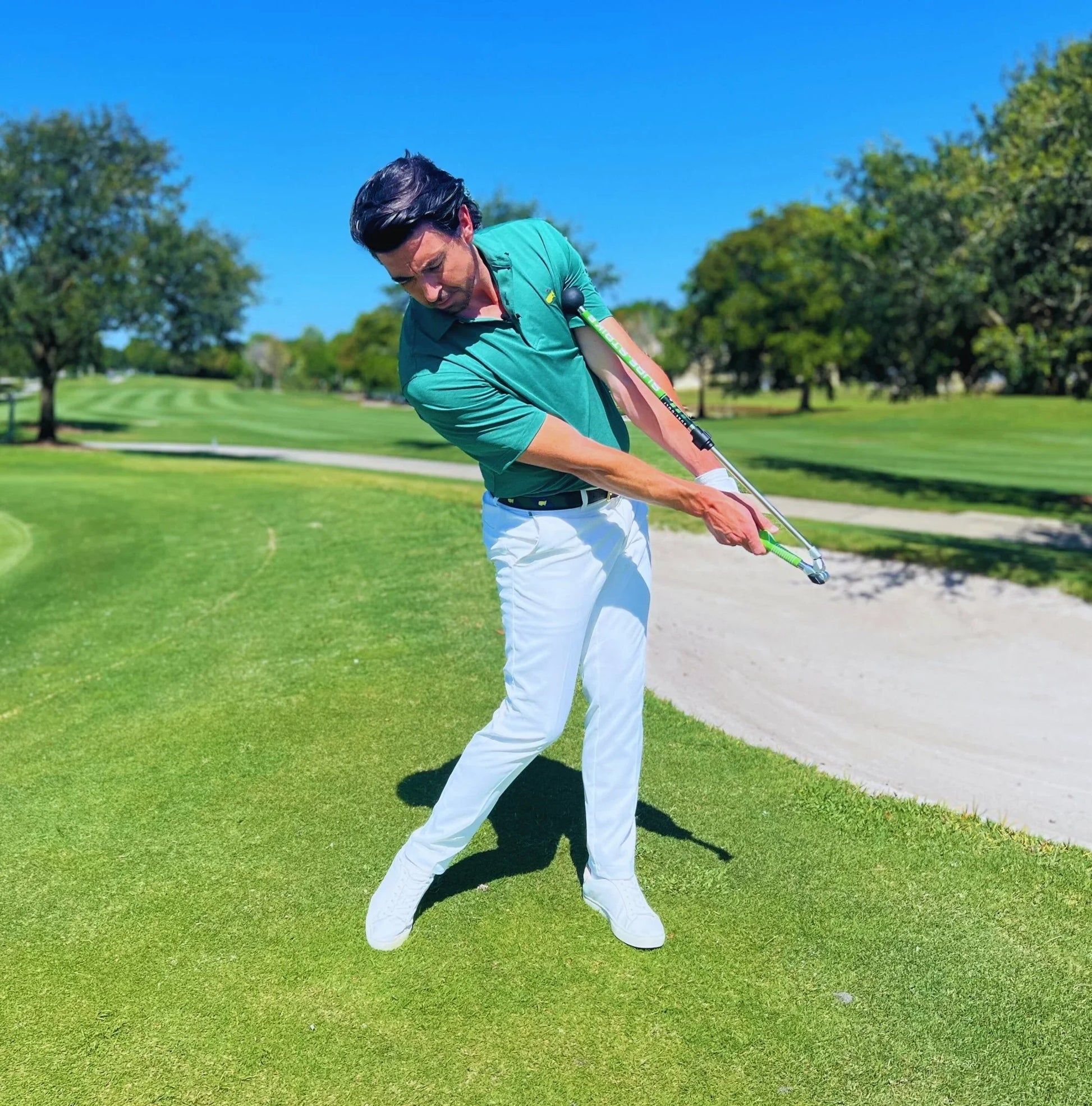 Man practicing golf swing using Sure Strike training aid on sunny golf course
