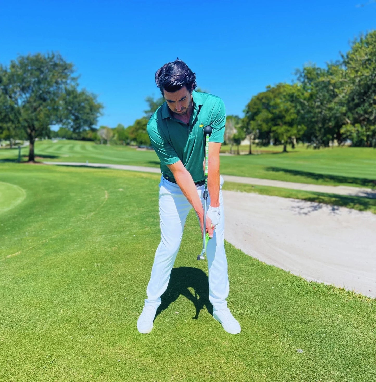 Man practicing golf swing with Sure Strike training aid on golf course under blue sky