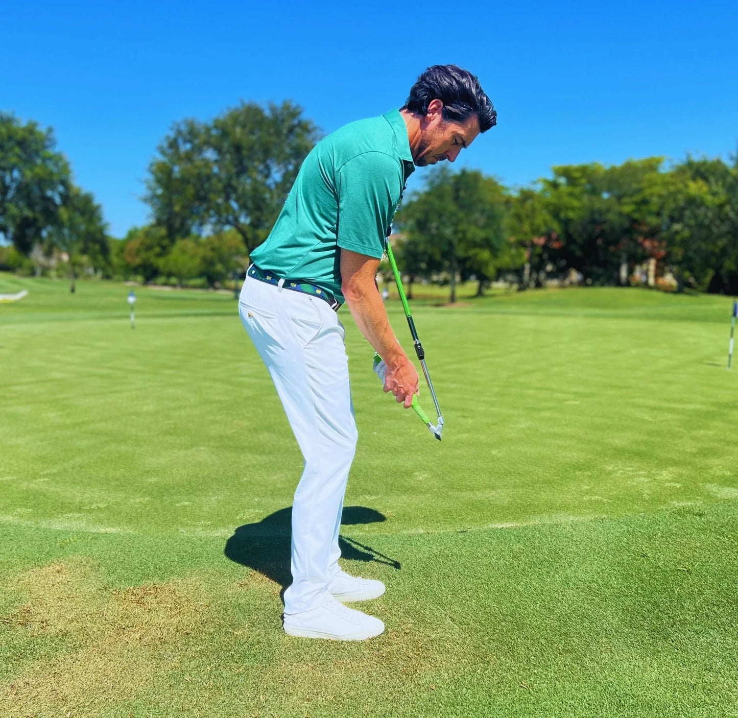 Man in green shirt and white pants using Sure Strike golf training aid on green golf course