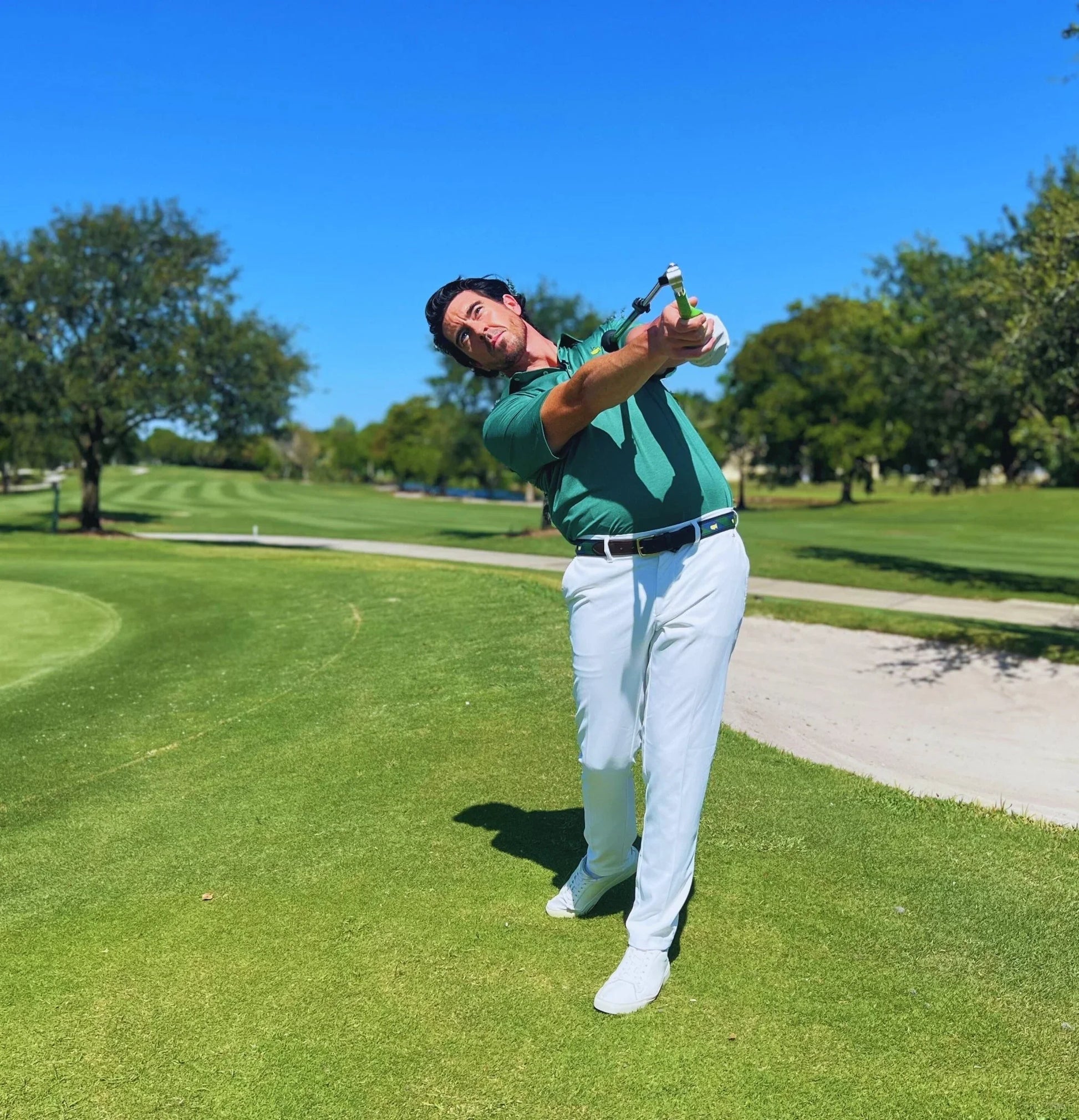Golfer practicing swing with Sure Strike training aid on sunny golf course green