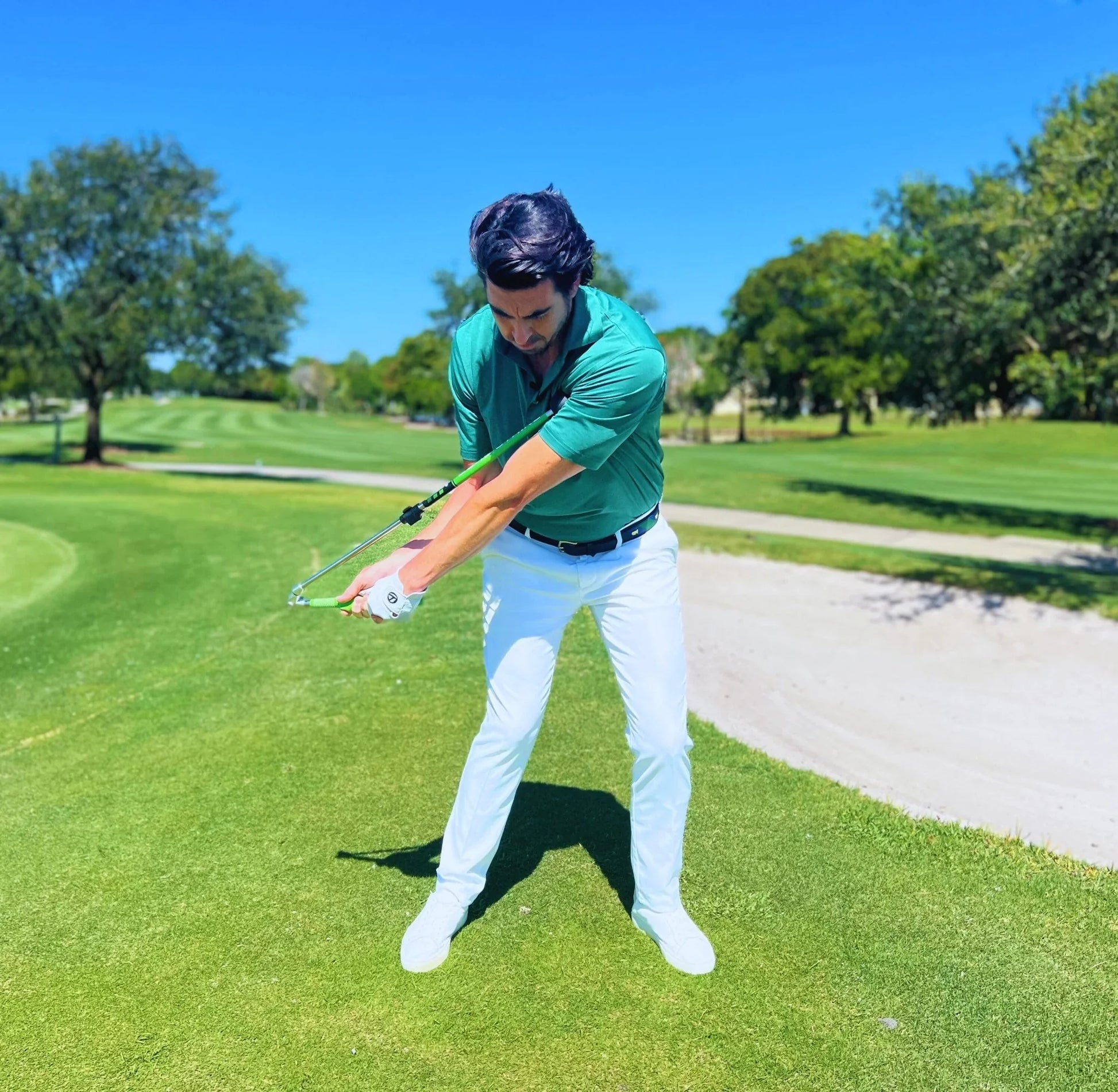 Golfer using Sure Strike training aid on green golf course under clear blue sky