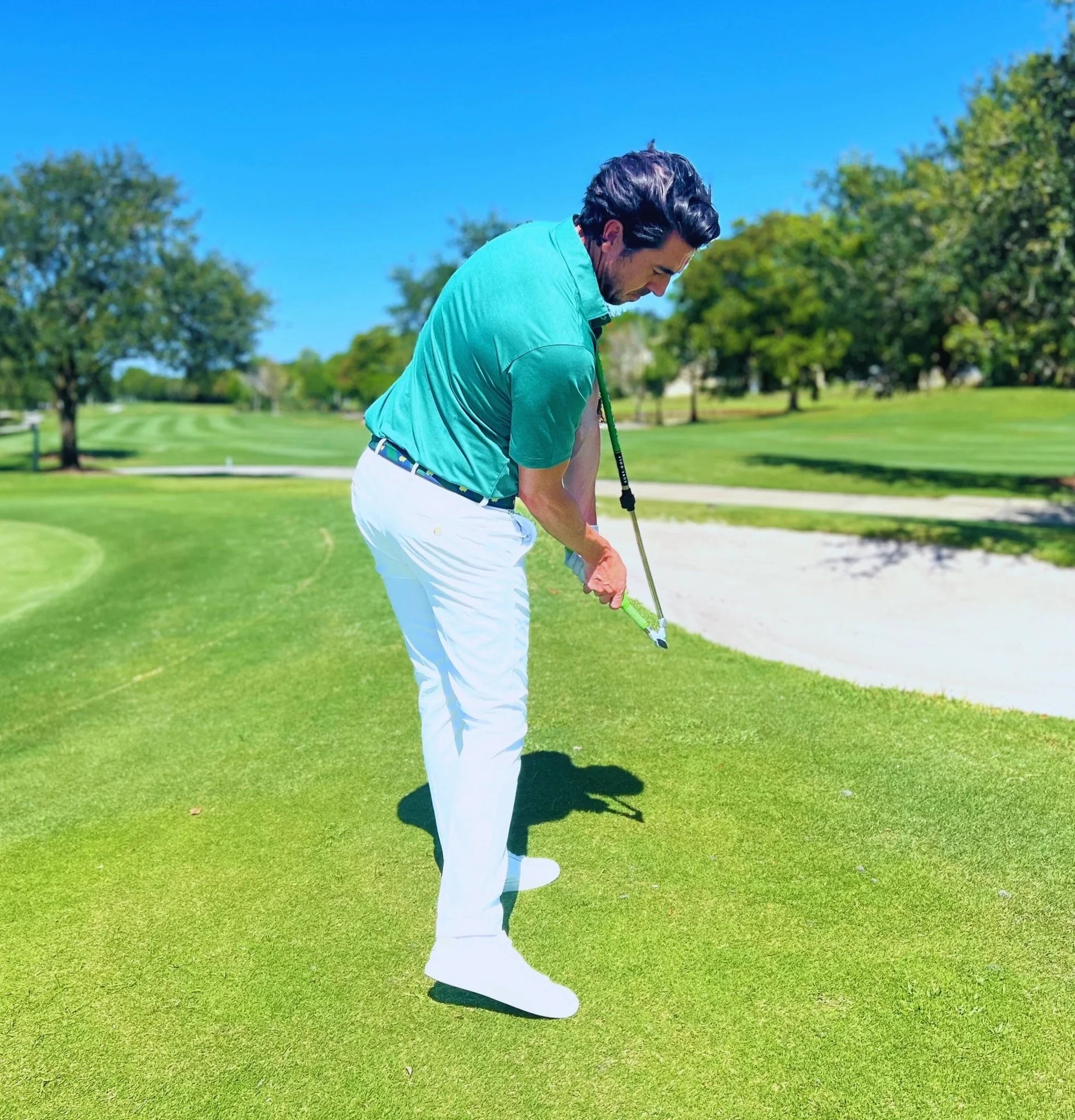 Golfer on lush green course using Sure Strike golf training aid near sand bunker