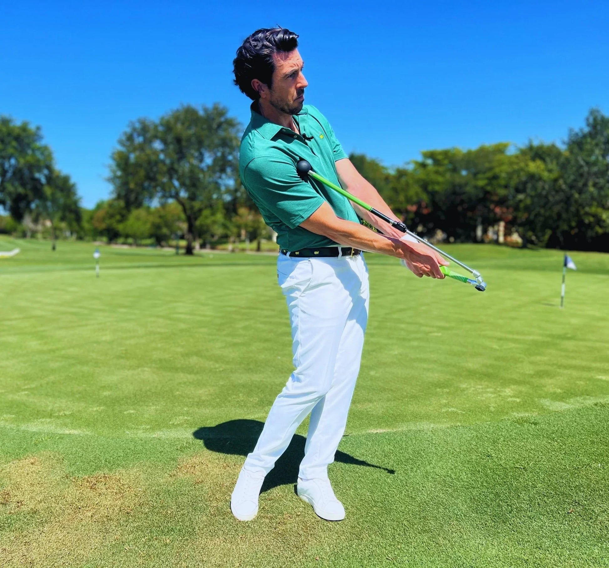 Man in green shirt using Sure Strike golf training aid on green golf course under clear blue sky