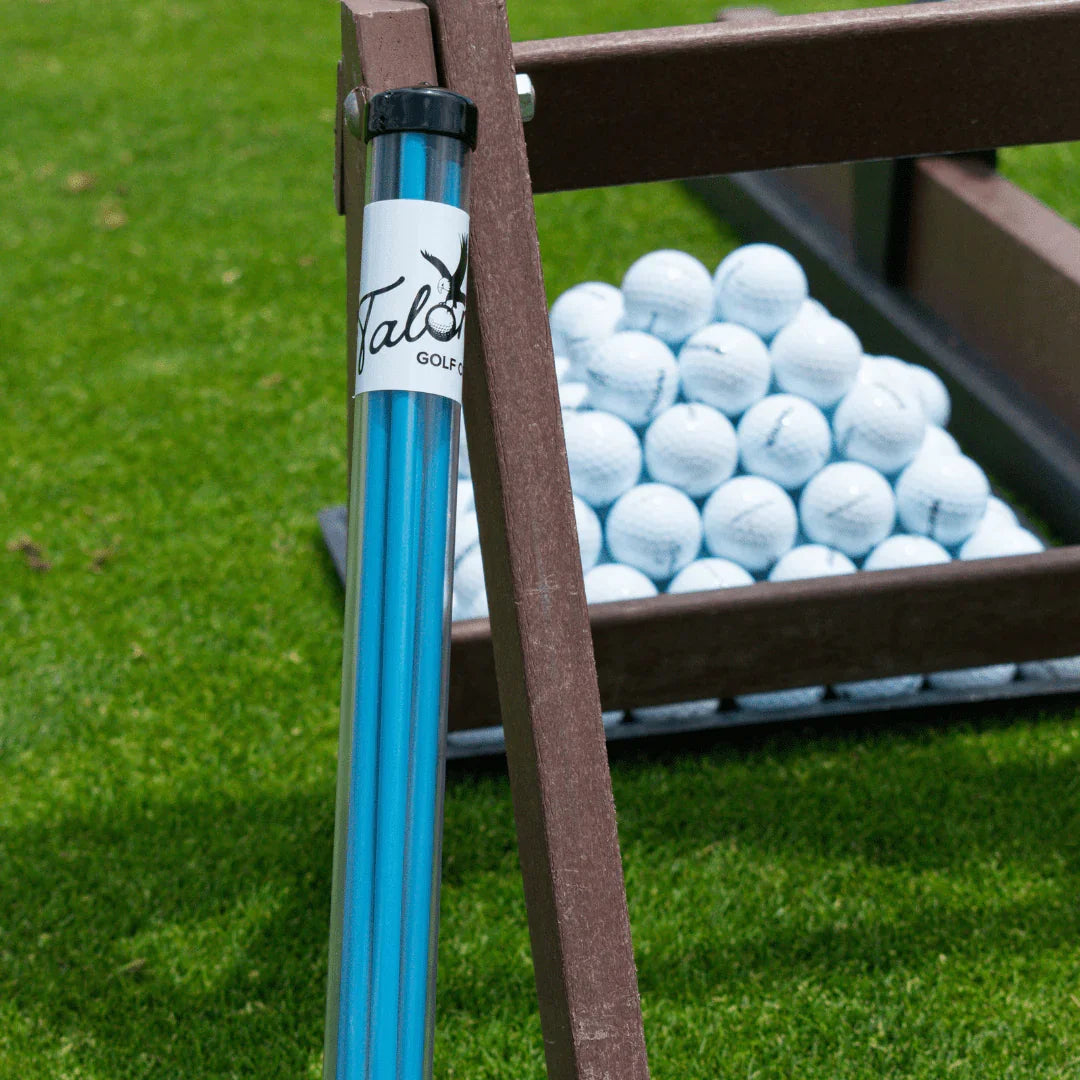 Blue Talon Golf alignment sticks next to a wooden rack filled with white golf balls on green grass