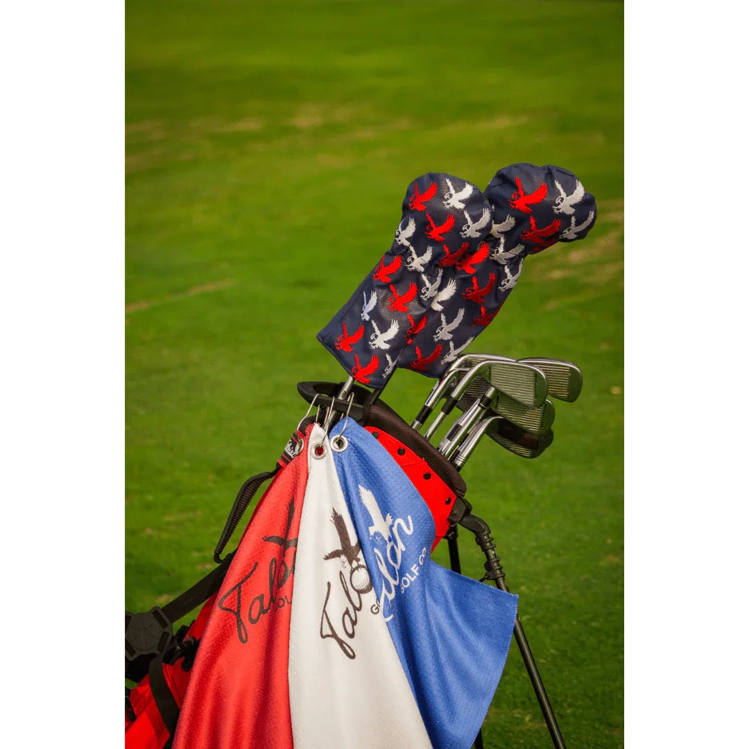 Red golf bag with clubs, Talon Utility golf towels in red, white, blue, and bird-patterned headcovers on grass
