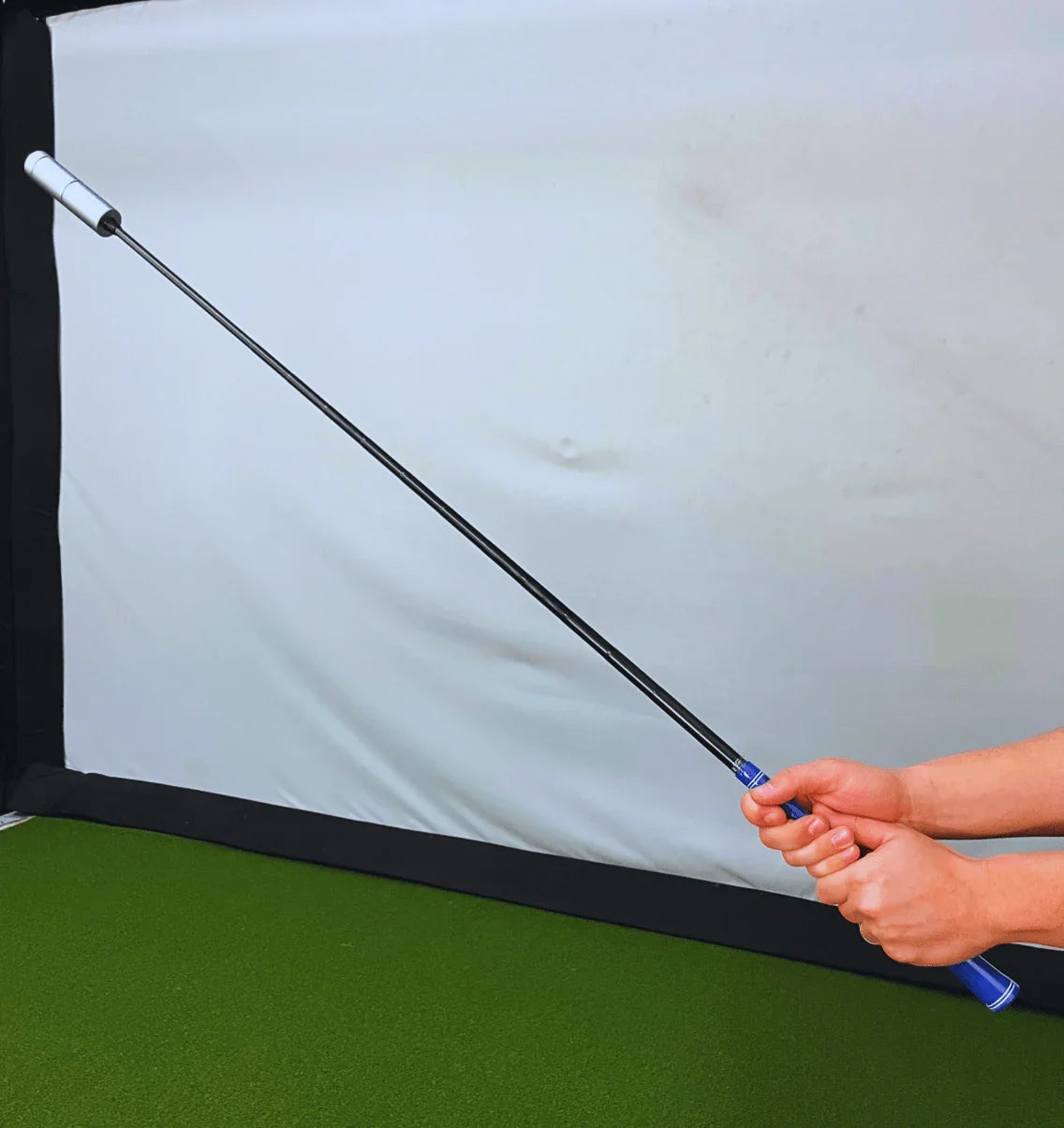 Person holding a flexible golf swing trainer rod on green mat with white backdrop