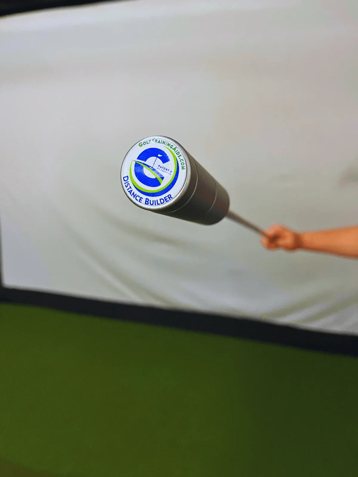 Golf training aid Distance Builder held indoors on green turf background