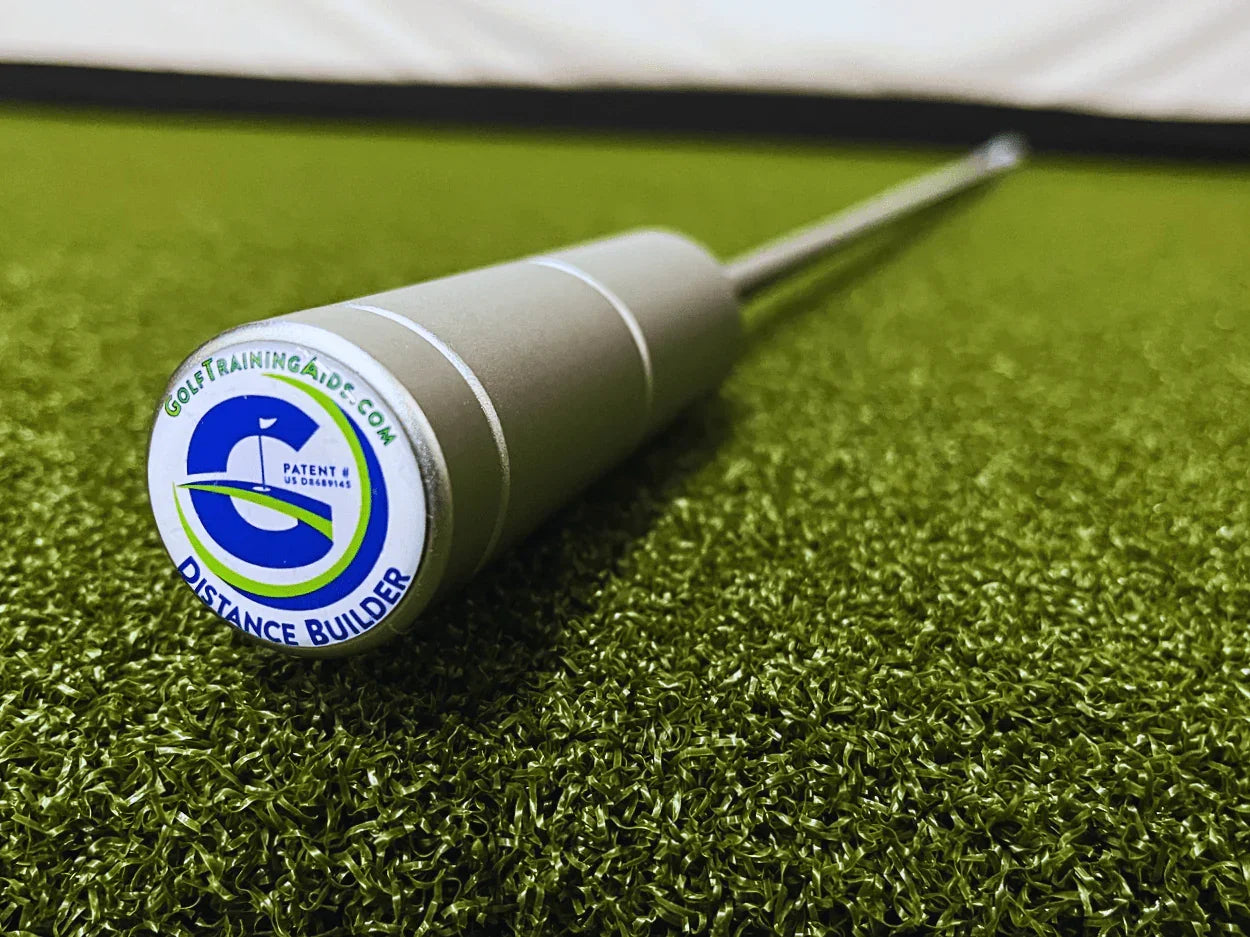 Close-up of a silver golf training aid called Distance Builder lying on artificial green turf