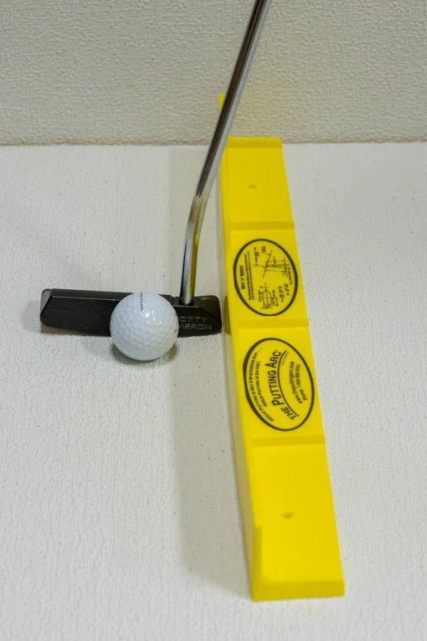Golf putter aligning a golf ball next to a bright yellow putting arc aid for golf practice