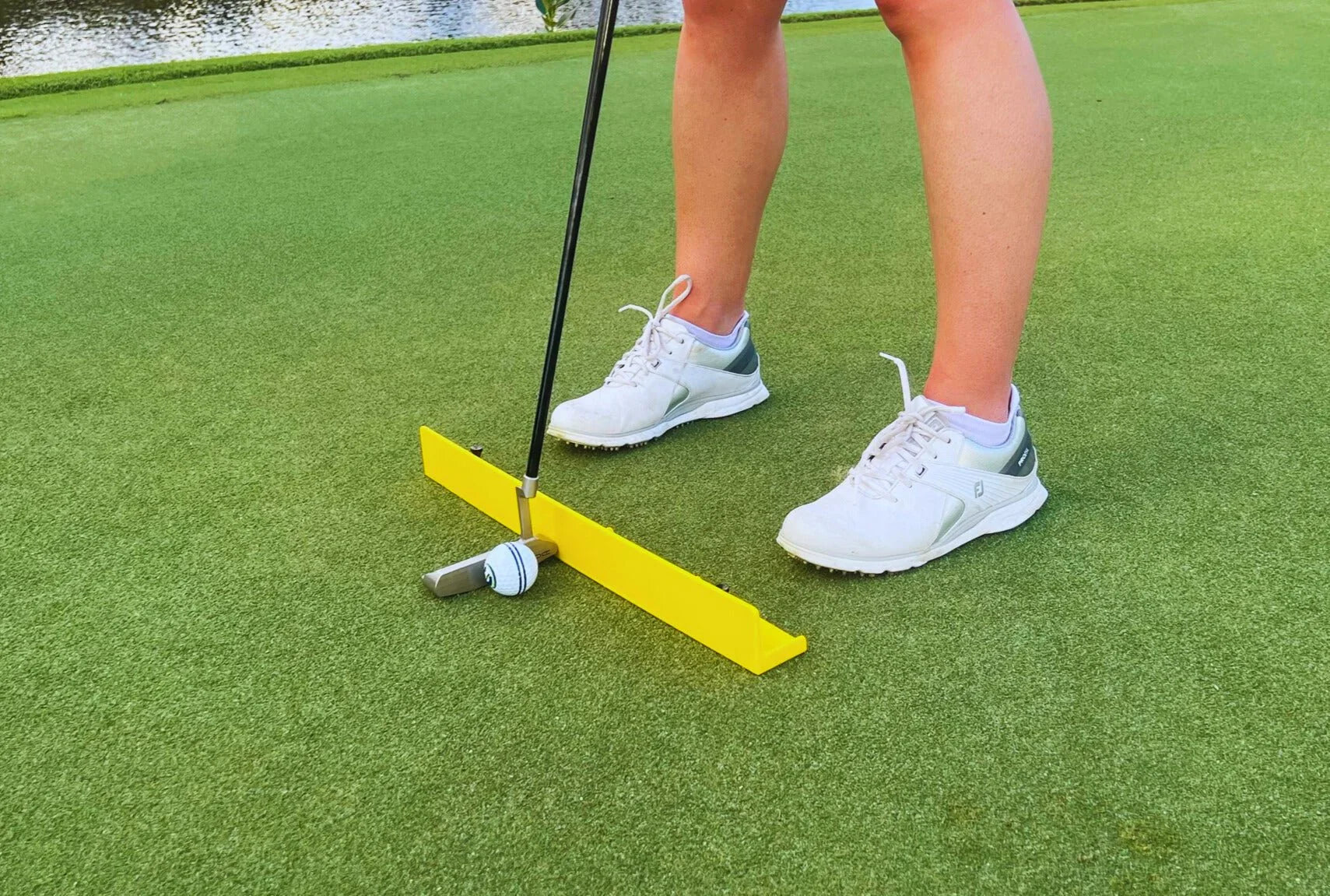 Golfer using a yellow putting arc training aid on green with white golf shoes and ball