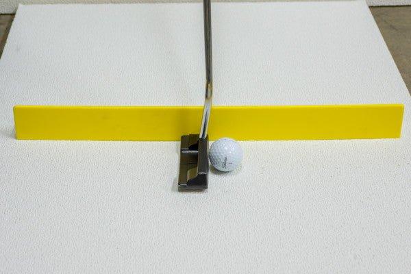 Golf putting training aid with a yellow alignment bar, metal putter, and golf ball on white surface