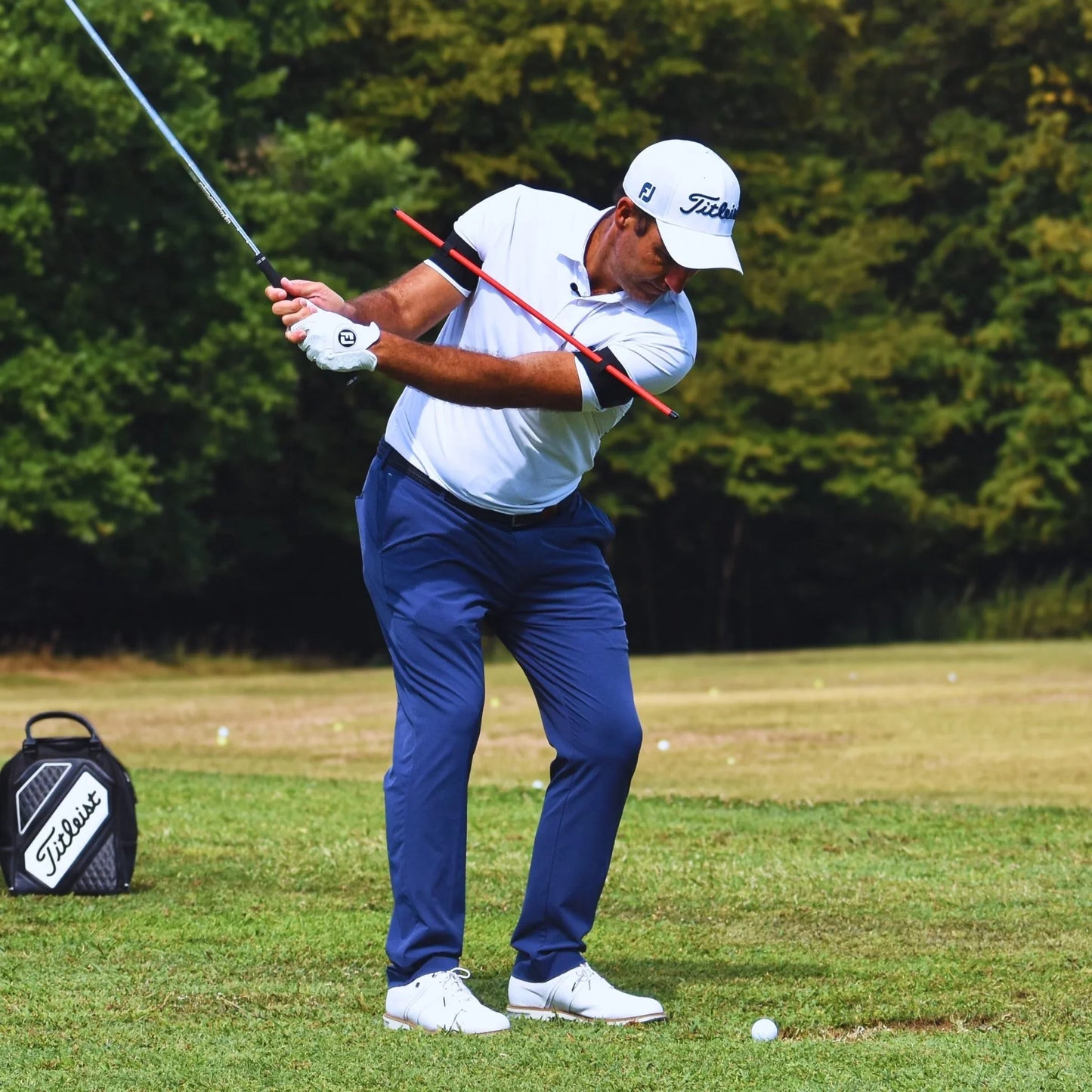 Golfer in white shirt and blue pants practicing swing on grass field with golf bag nearby