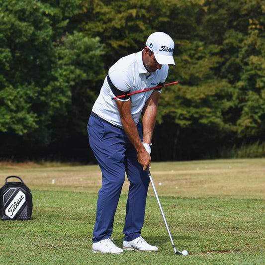Golfer in white cap and polo using orange swing trainer on green golf course with Titleist bag