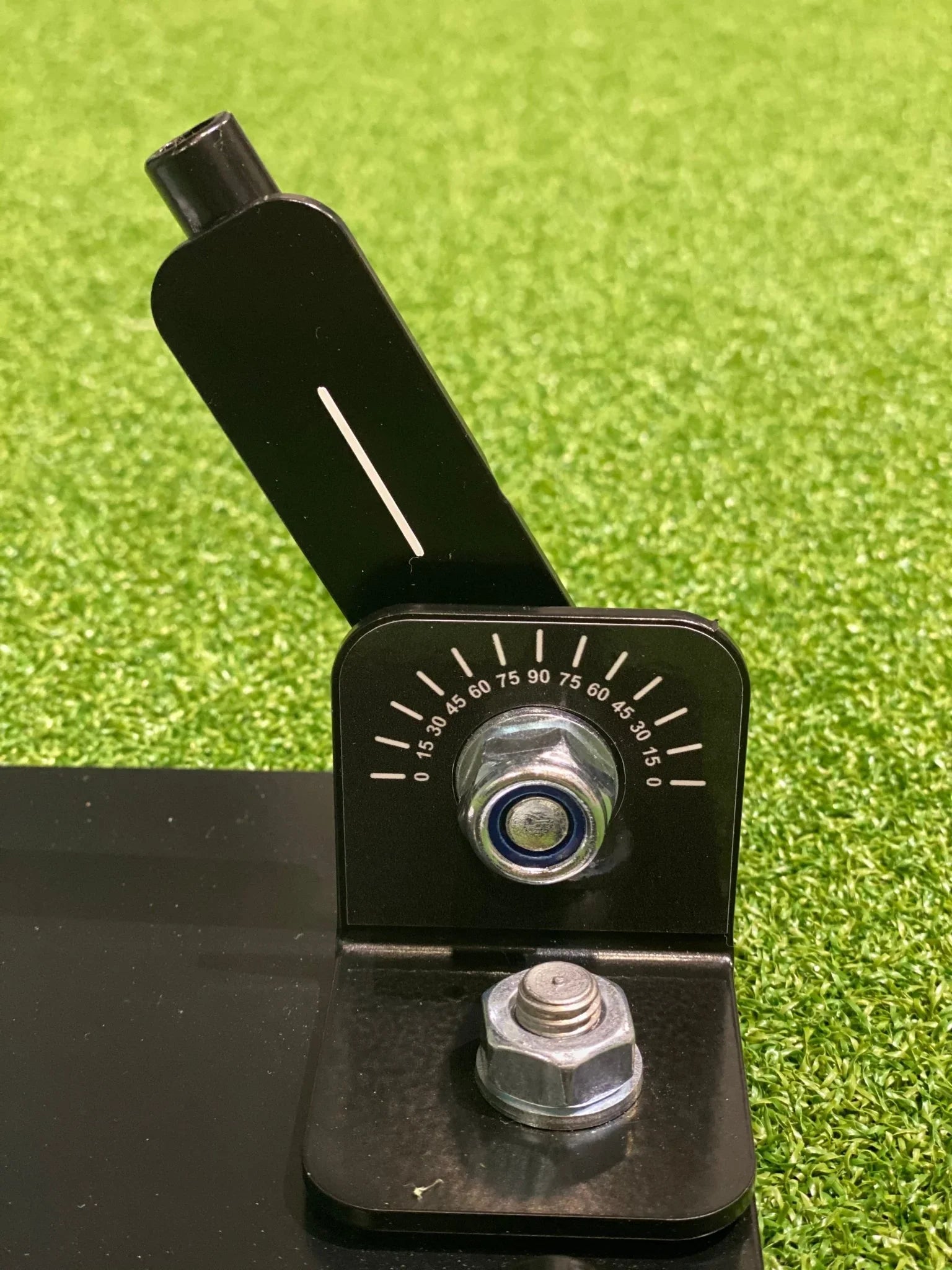 Close-up of black metal swing plate base with angle adjustment dial and bolts on grass surface