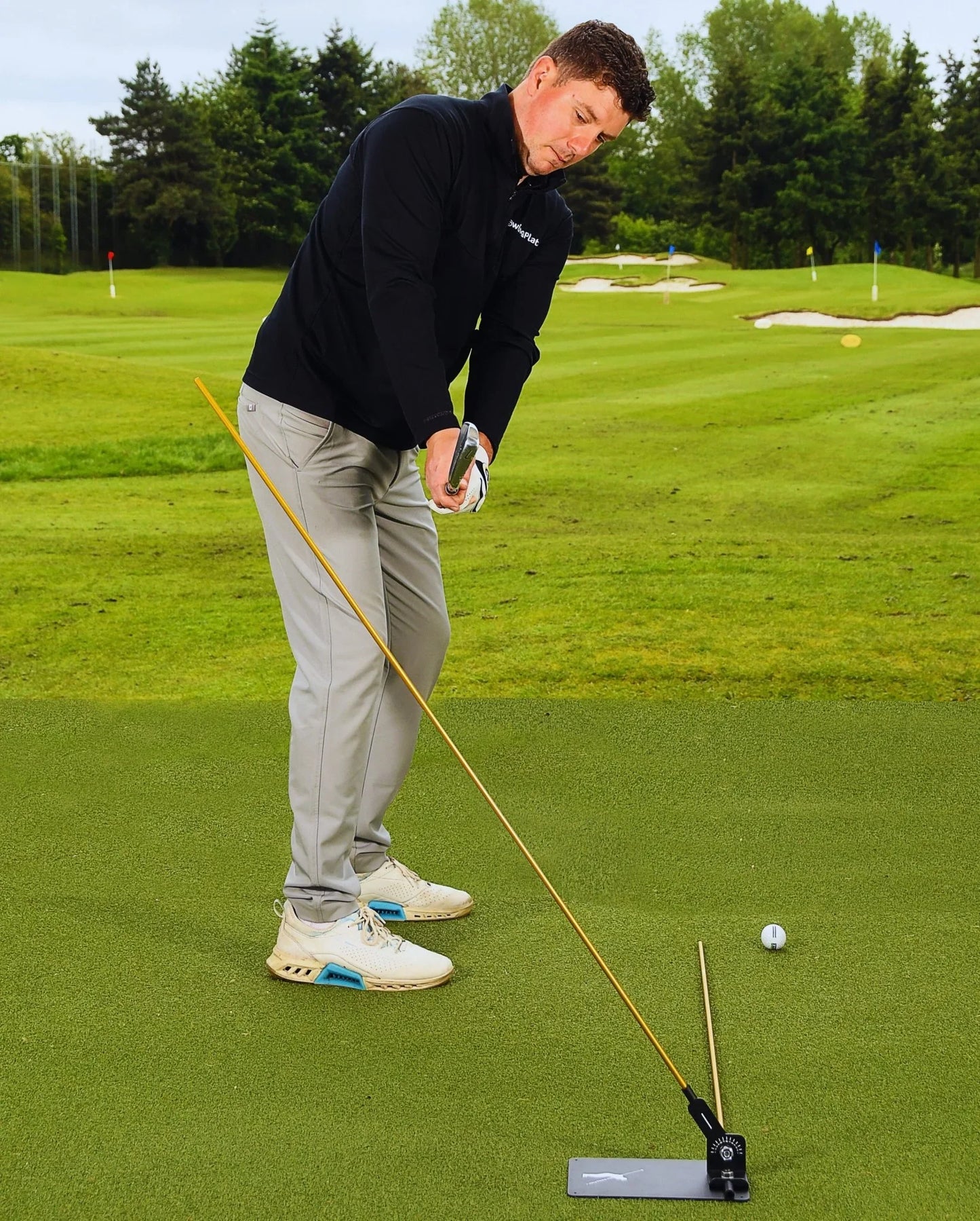 Golfer practicing swing with a training plate and rod on green golf course