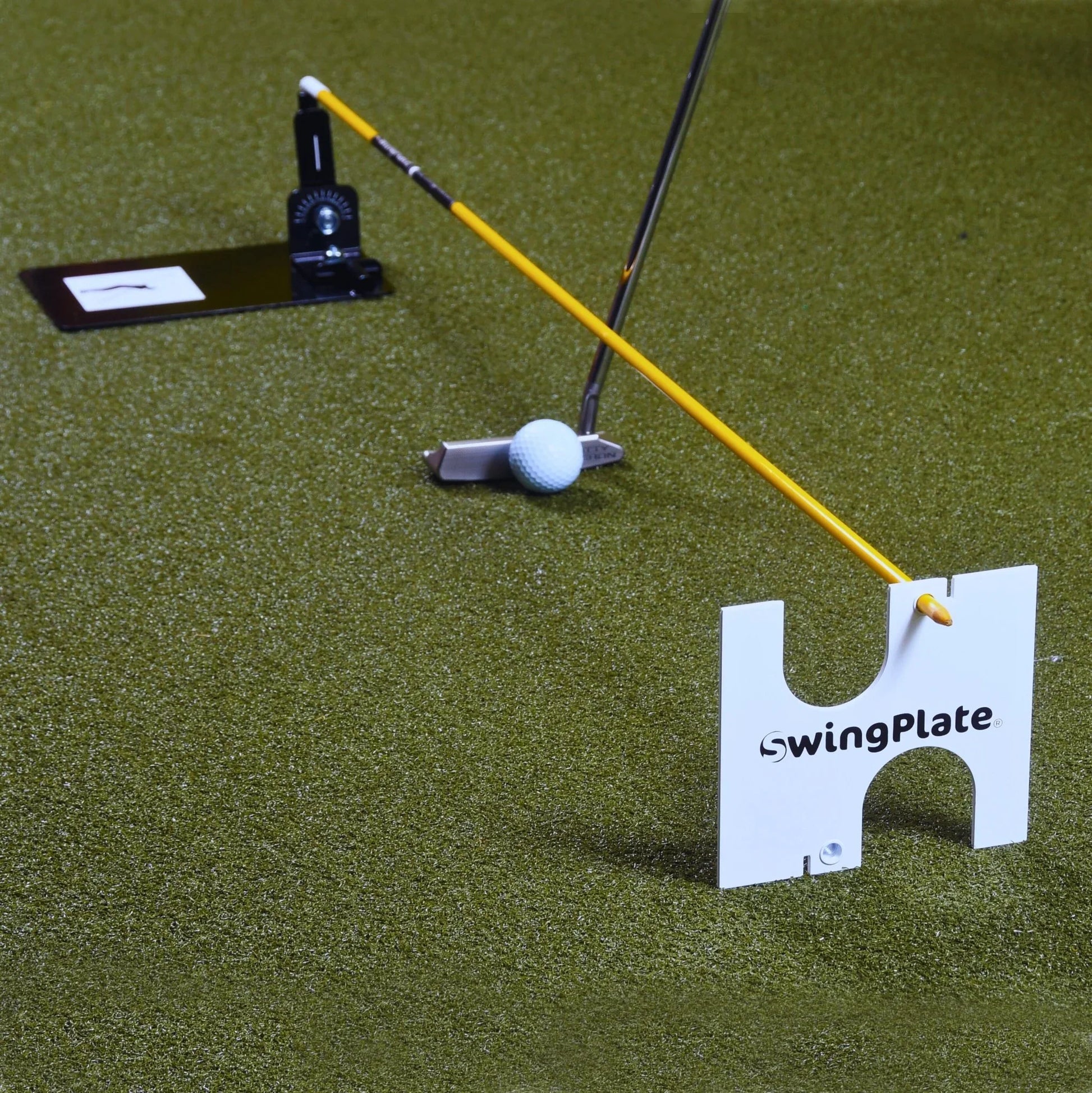 Golf putting training aid SwingPlate on green turf with putter, golf ball, and alignment stick
