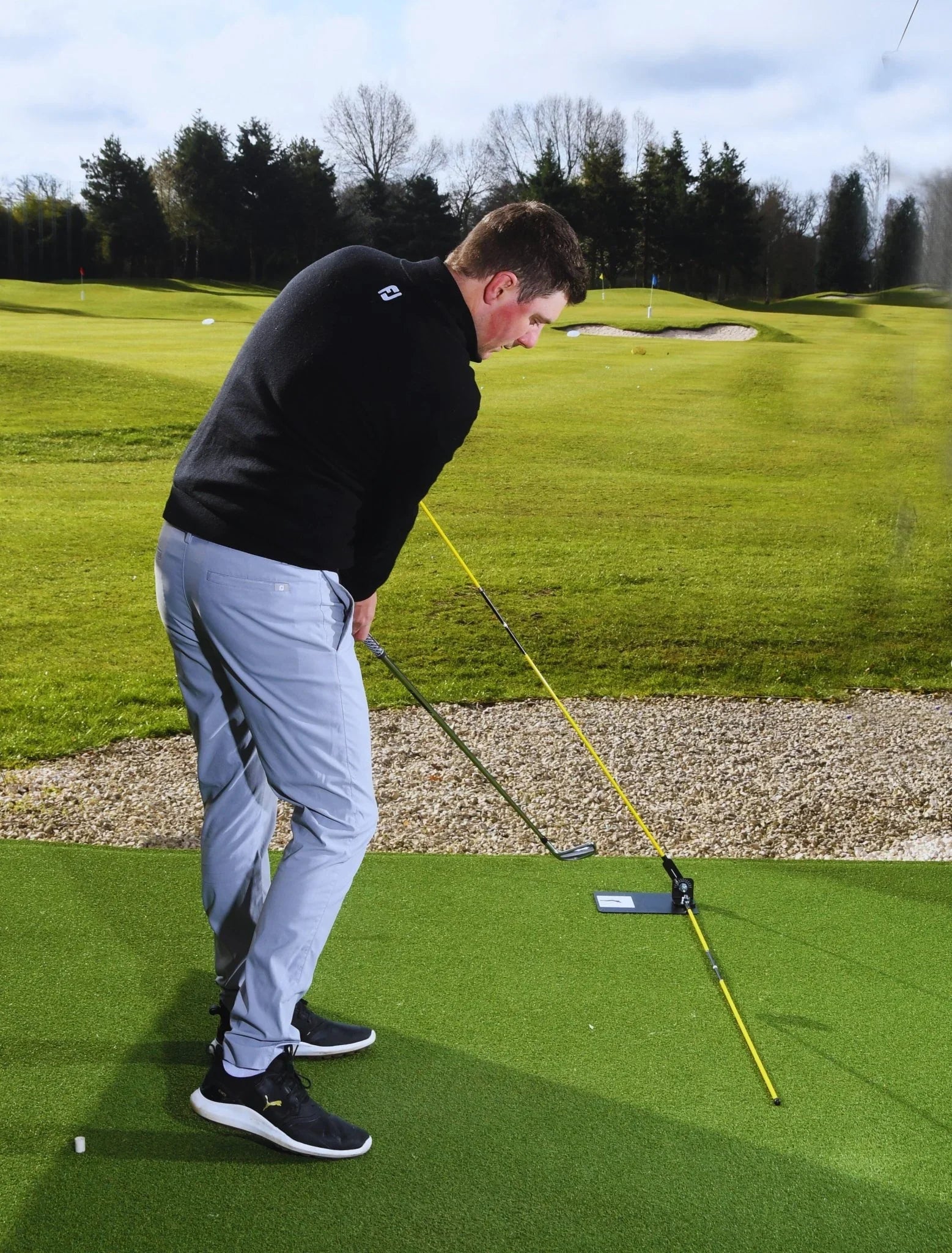 Golfer practicing swing on green turf with yellow swing training aid on sunny golf course