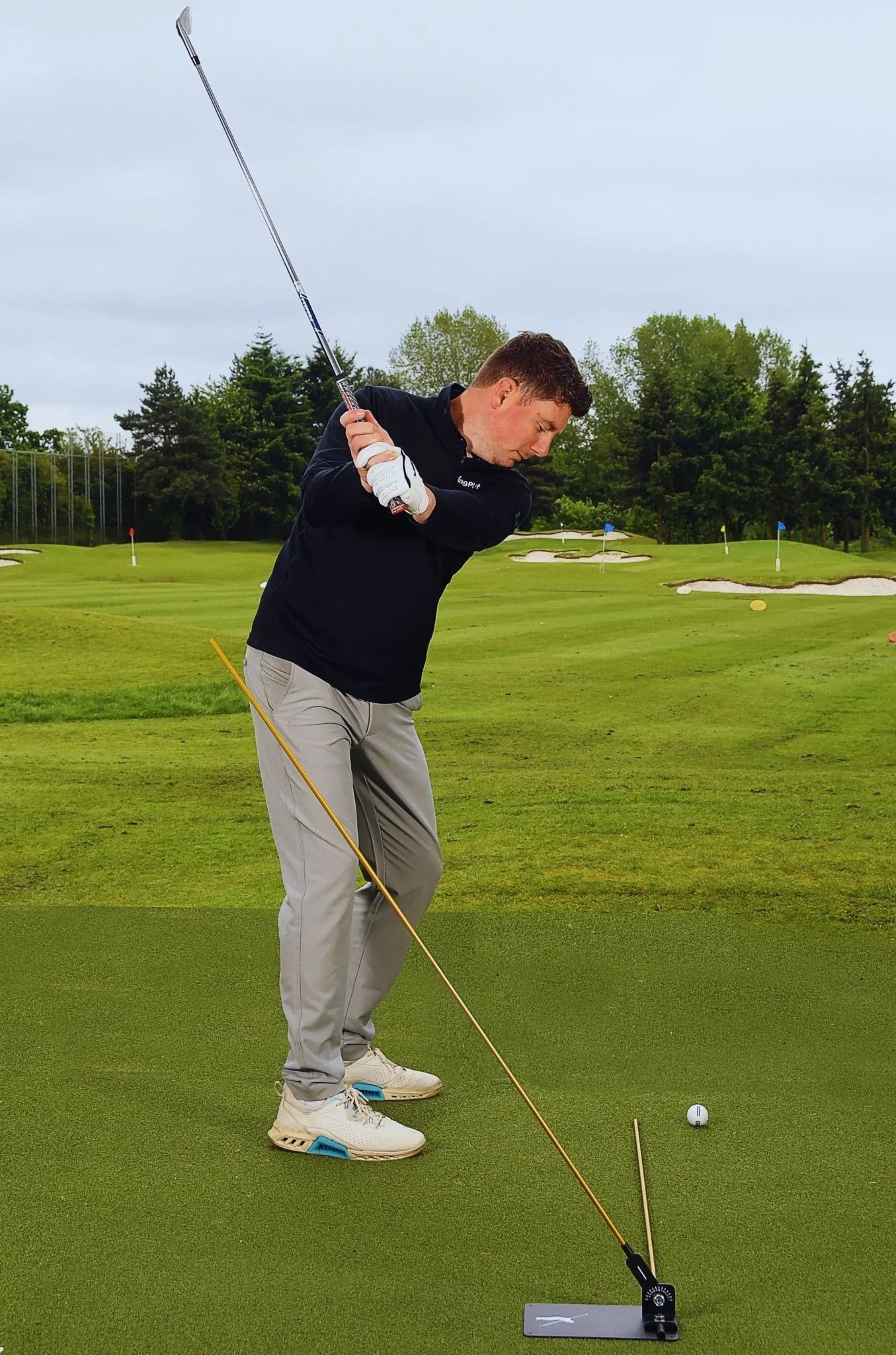 Golfer practicing swing on green with swing plate trainer and golf ball on training mat