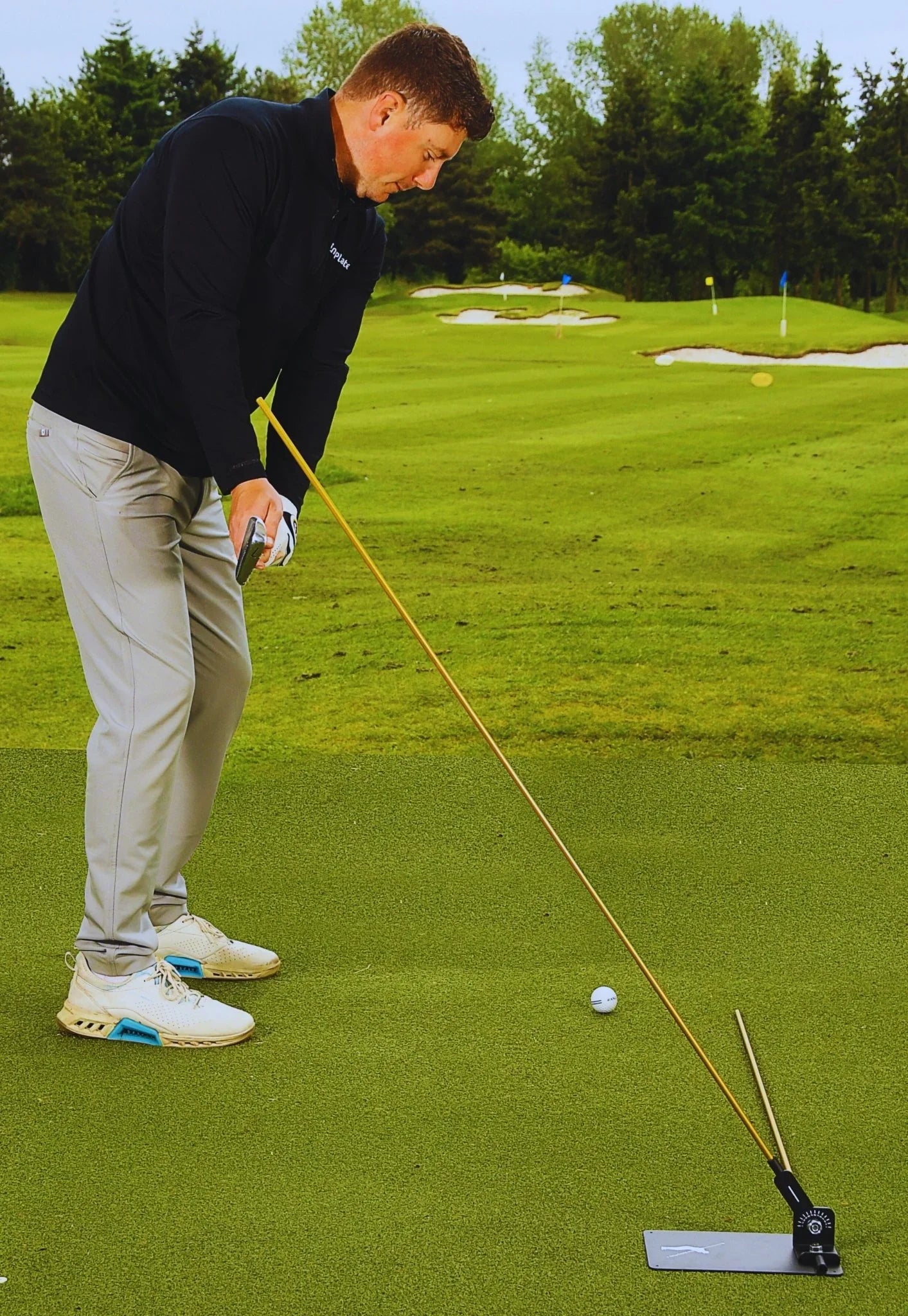 Golfer practicing putting stroke with The Swing Plate base and alignment stick on green golf course
