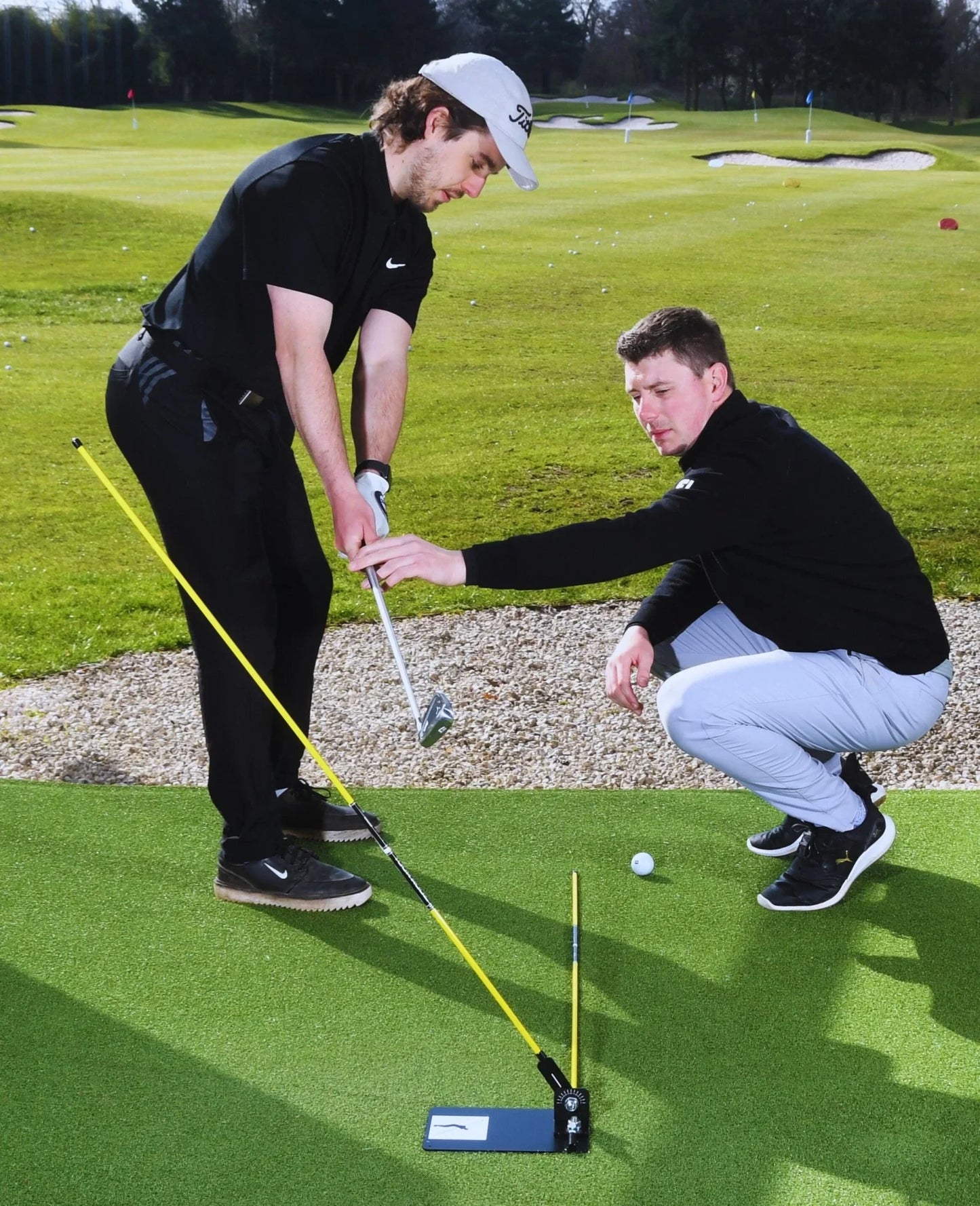 Golf lesson on putting green with instructor guiding player using swing plate training aid
