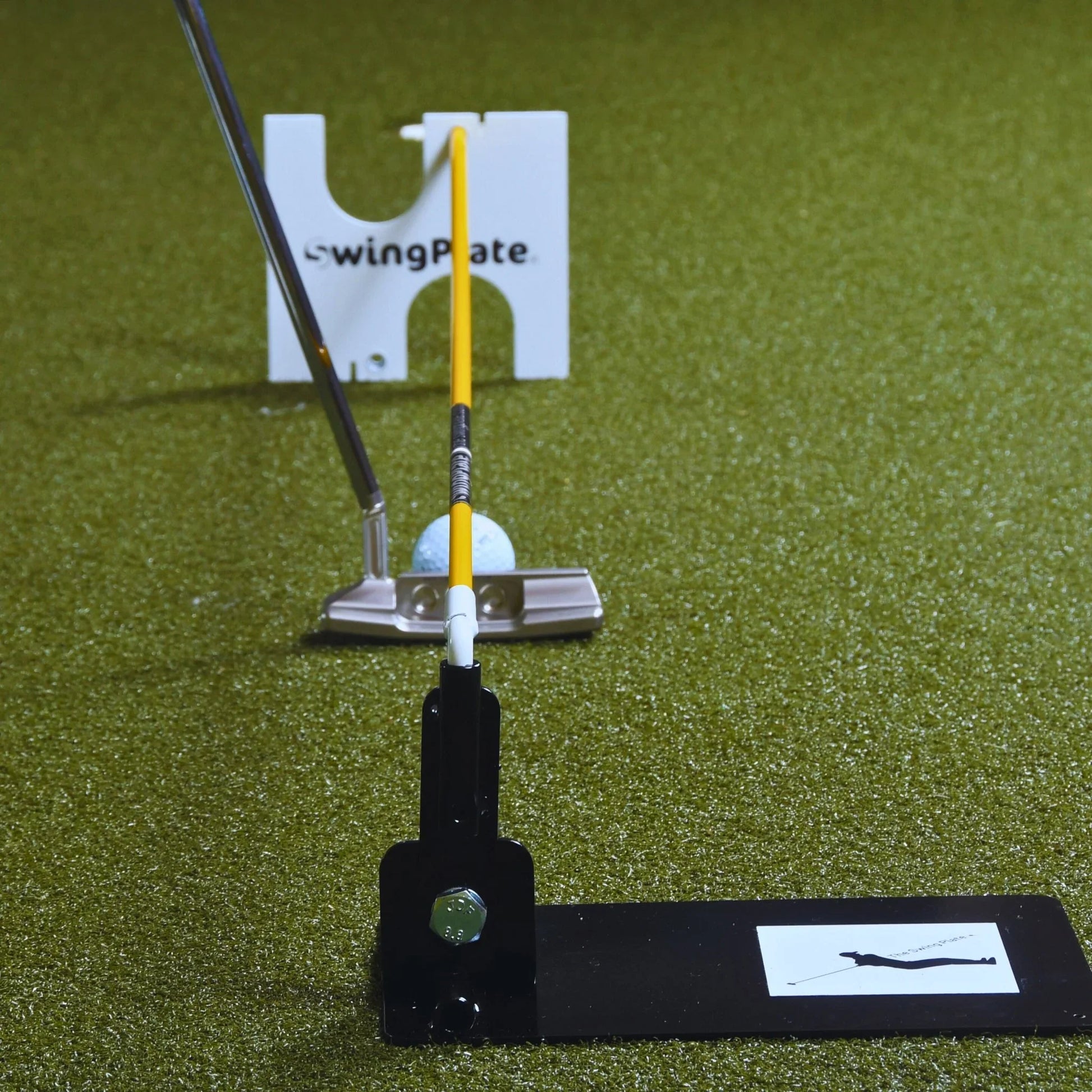Golf putting training aid SwingPlate with yellow alignment stick and putter on green turf