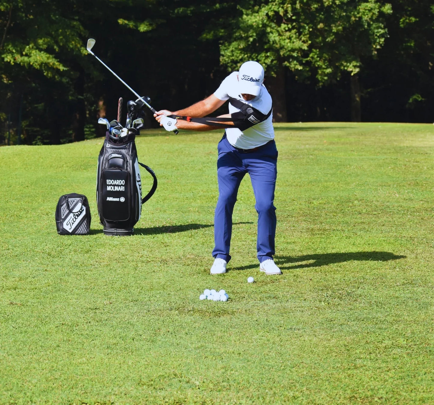 Golfer wearing swing trainer practicing on green with golf bag and balls on sunny day